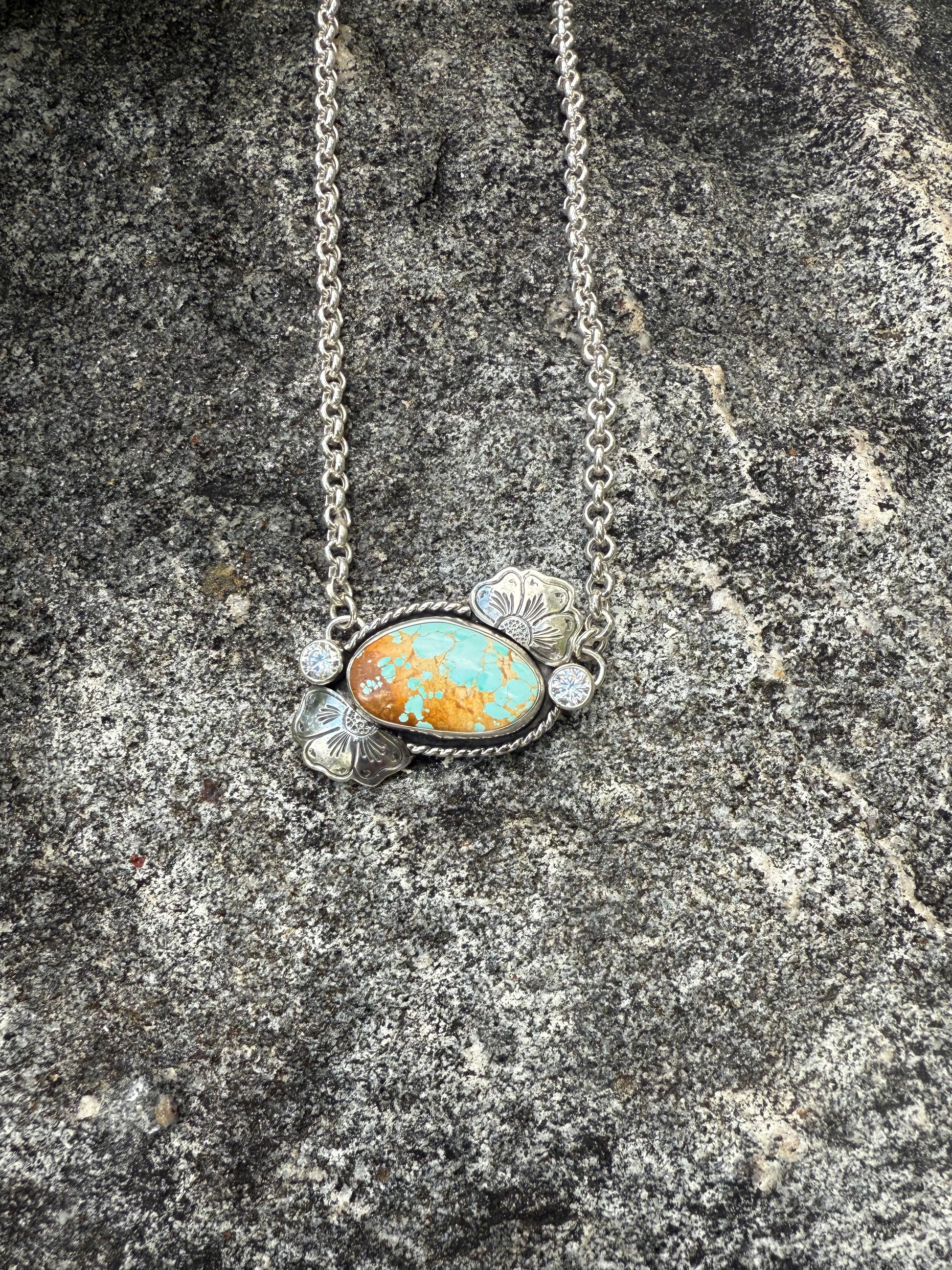 Necklace with a turquoise and gold pendant on a stone surface