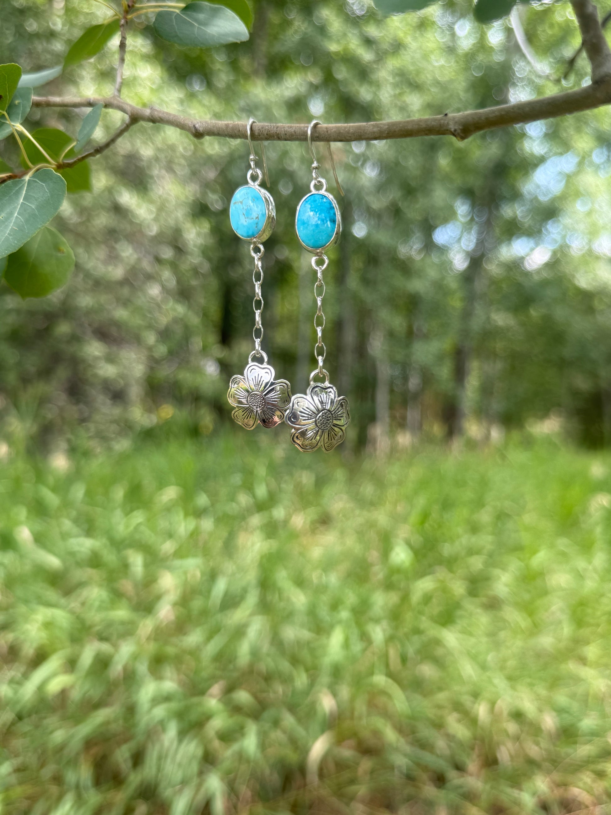Silver earrings with turquoise stones hanging from a branch in a natural setting