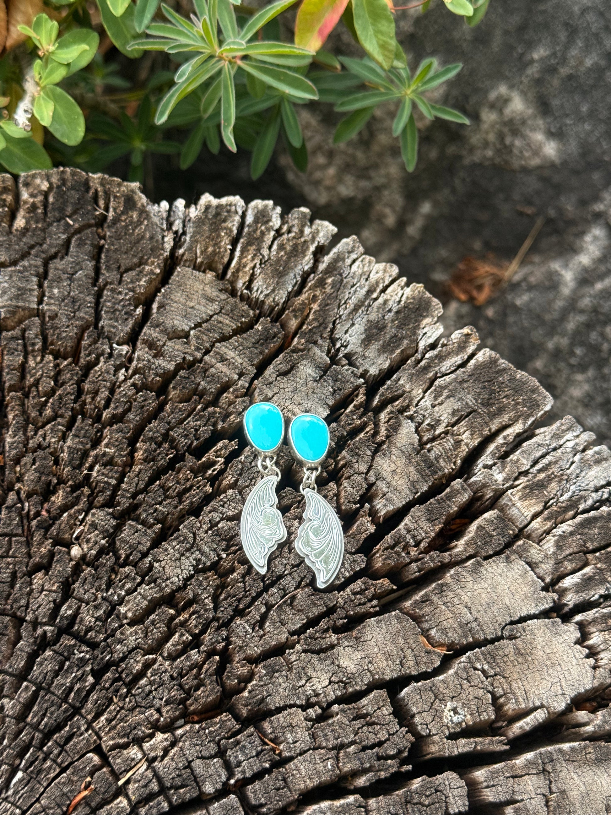 Pair of earrings with turquoise stones and silver designs on a textured wooden surface.